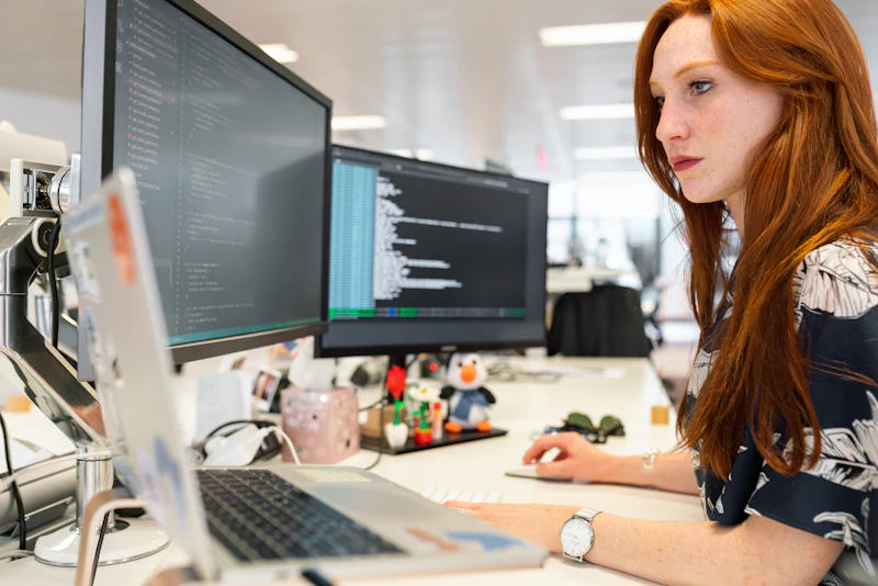 Ontwikkelaar werkt geconcentreerd aan code op twee schermen